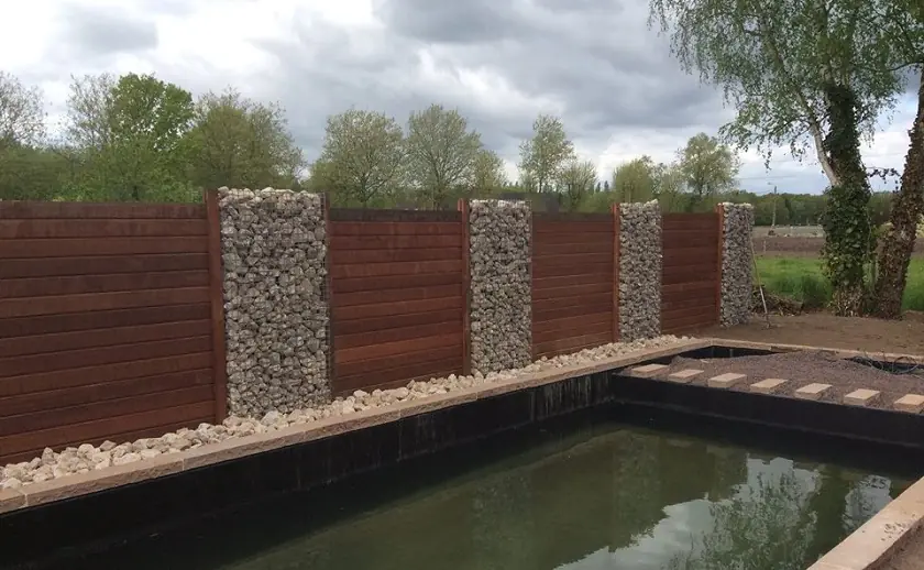 Houten wand met schanskorven achter de zwemvijver